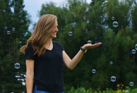 En un espacio abierto con árboles de fondo, mujer sostiene con su mano izquierda una burbuja