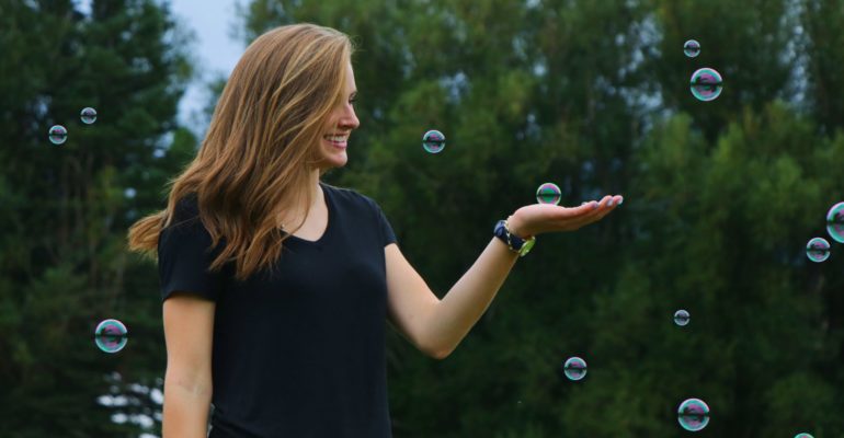 En un espacio abierto con árboles de fondo, mujer sostiene con su mano izquierda una burbuja